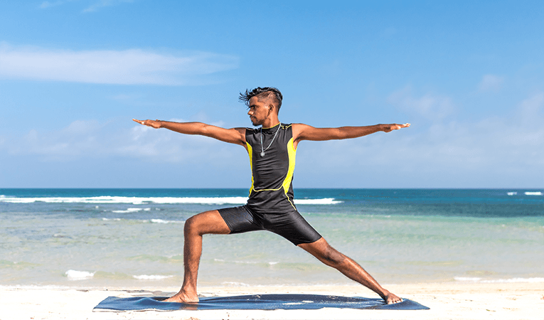 Man doing yoga on the beach with blue skies