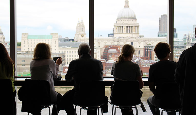 silhouettes of business-people sitting in front of full length windows looking out on London