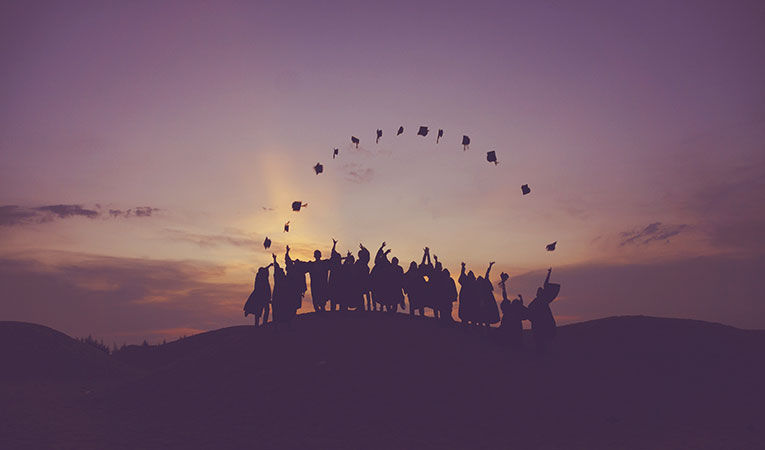 Group of graduates throwing hats into sky against sunset