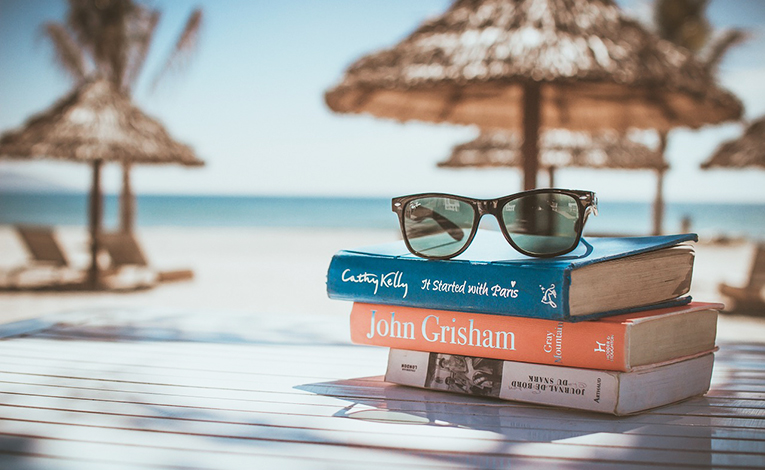  Stack of books and glasses at beach.