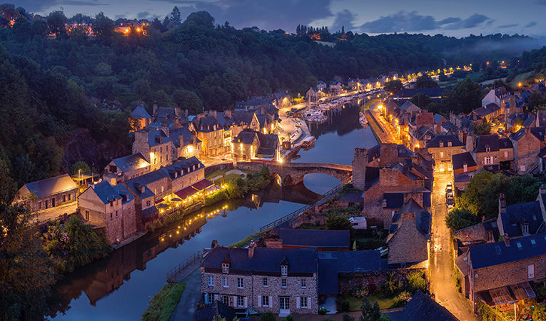 Dinan, Francia, ciudad iluminada por la noche a lo largo de la orilla del río