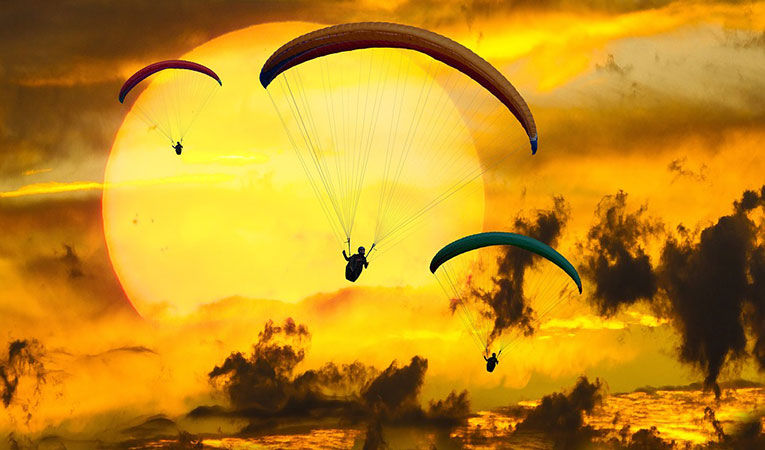 Paragliders glide in front of a huge yellow sun
