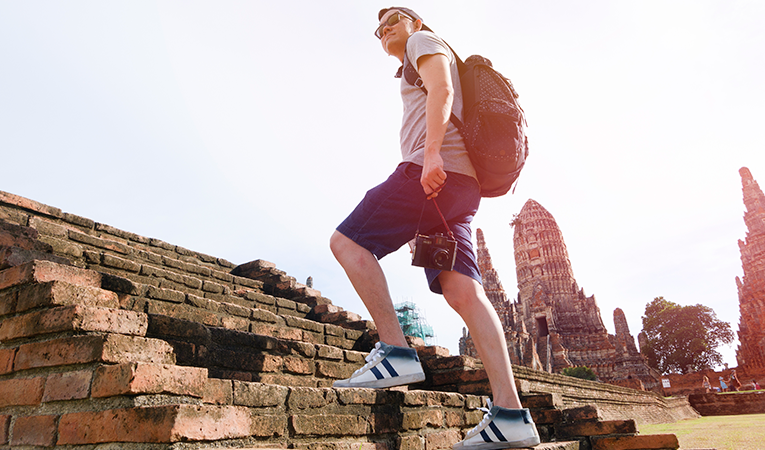 young man walking up the steps of ancient temple with backpack and camera
