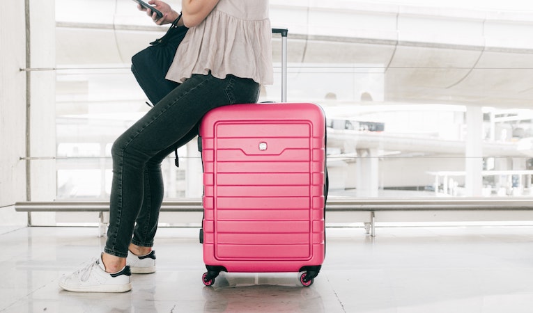 person sitting on a pink suitcase in an airport